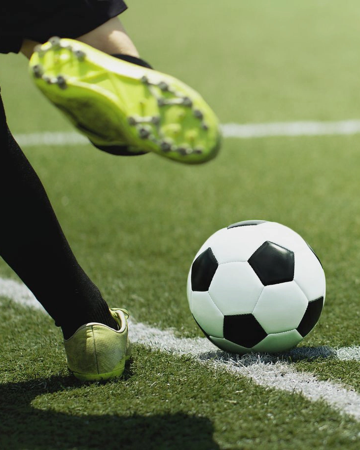 Nahaufnahme des Beins und Fußes eines Fußballspielers der SpVg 0507 Odenkirchen, der einen schwarz-weißen Ball auf grünem Rasen kickt, wobei der Ball auf einer weißen Seitenlinie liegt.